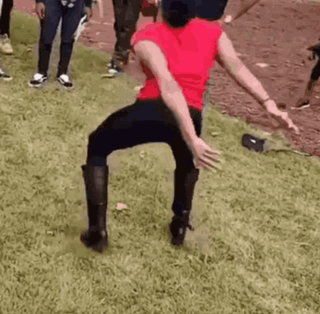 a woman in a red shirt and black boots is dancing in the grass