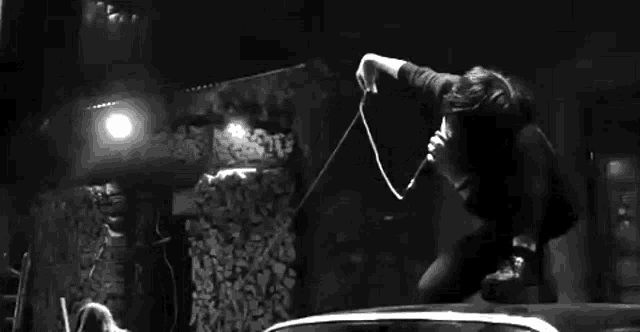 a black and white photo of a person jumping over a car roof holding a microphone .