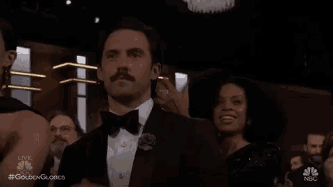 a man in a tuxedo with a mustache is applauding while sitting in a crowd .
