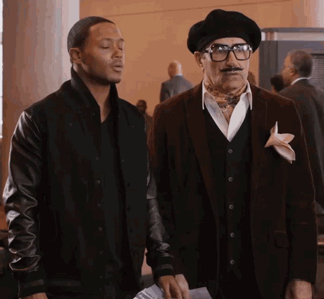 two men standing next to each other with one wearing glasses