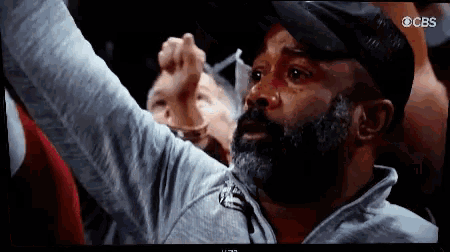 a man with a beard is watching a cbs broadcast