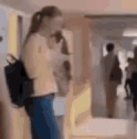 a woman with a backpack is standing in a hallway holding a dog .