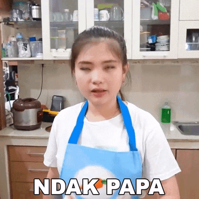 a woman wearing an apron is making a funny face in a kitchen with the words ndak papa written on the bottom