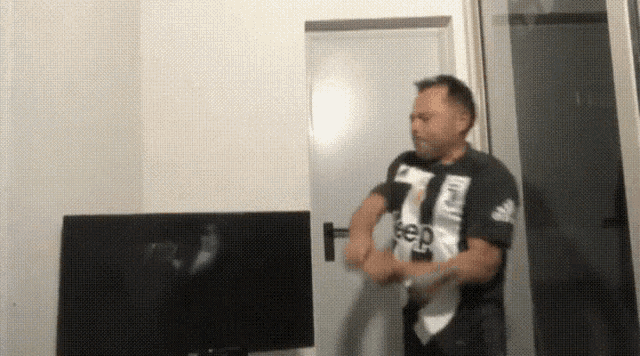 a man in a jeep shirt is standing in front of a flat screen tv