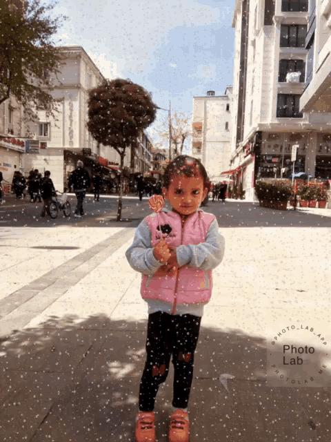 a little girl in a pink jacket is holding a lollipop in her hand