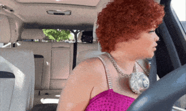 a woman with red hair is sitting in a car wearing a necklace