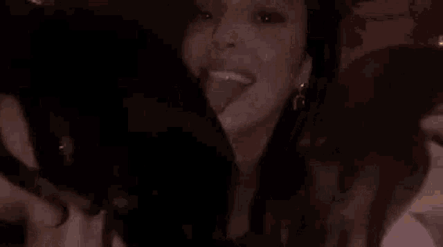 a woman is sticking her tongue out while taking a picture of herself in the dark .