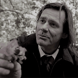 a man in a suit and tie is holding a flower in his hand in a black and white photo .