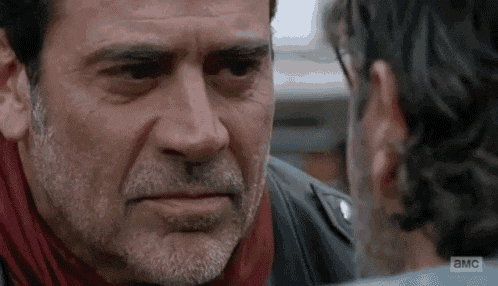 a man with a beard and a scarf is looking at another man 's face .