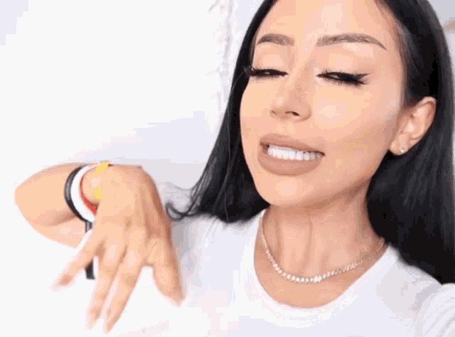 a woman wearing a white t-shirt and a pearl necklace is smiling