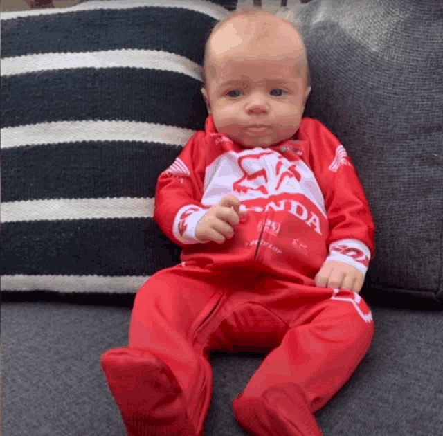 a baby wearing a red and white honda outfit sits on a couch