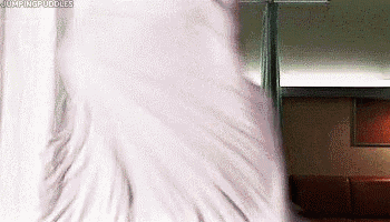 a person is laying on a bed in a living room with a white blanket .