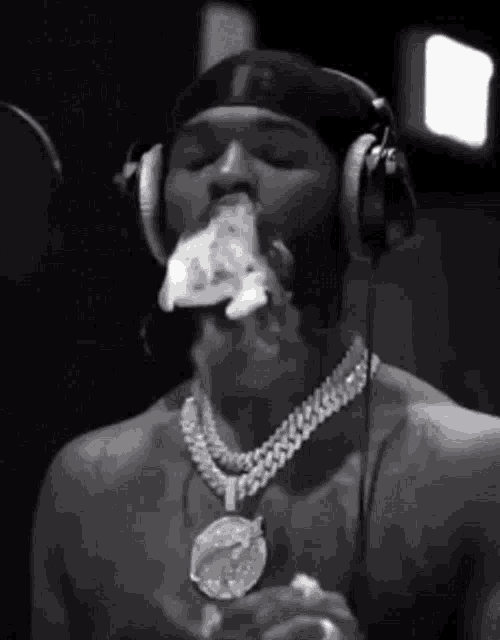 a black and white photo of a shirtless man wearing headphones and eating a slice of pizza .