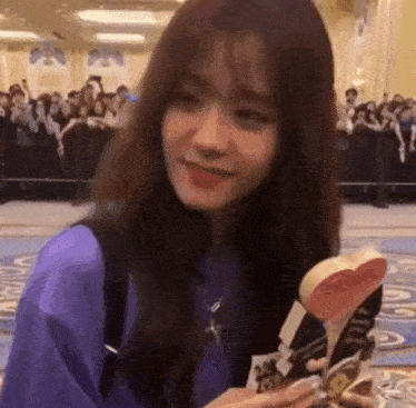 a woman in a purple shirt is holding a heart shaped object in her hands .
