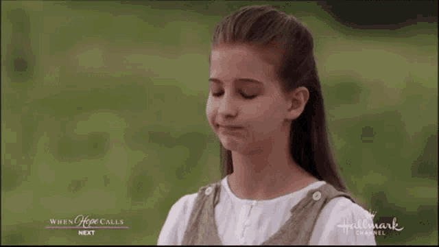 a young girl is standing in a field with her eyes closed and a hallmark channel advertisement behind her
