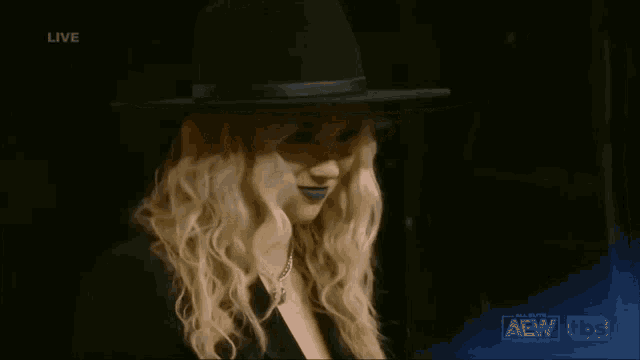 a blonde woman wearing a black hat is on a live aew tv show