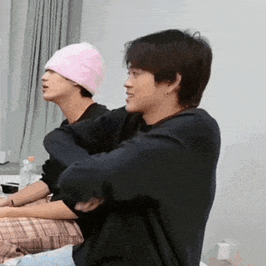 a man wearing a pink hat is sitting next to another man .