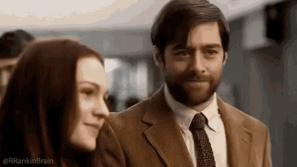 a man and a woman are standing next to each other in a room . the man is wearing a suit and tie .