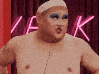 a drag queen without a shirt is standing in front of a neon sign that says k