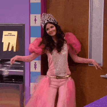 a woman in a pink dress with a crown on her head stands in front of a free compliments sign