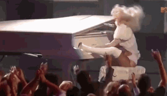 a woman is sitting on a piano in front of a crowd with her legs up .