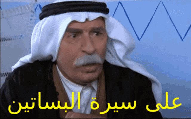 a man wearing a turban and a white scarf has arabic writing on the bottom right