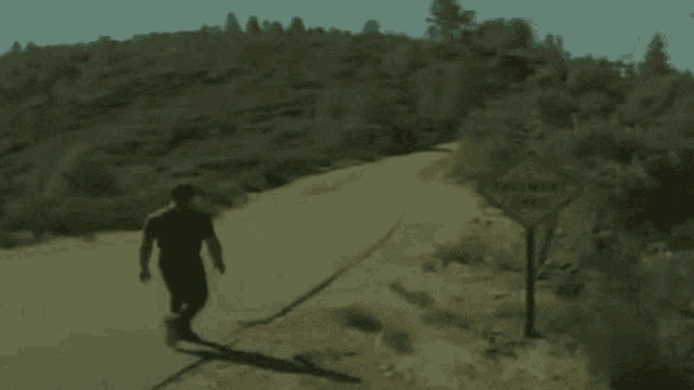 a man walks down a dirt road next to a yellow sign that says pavement ends
