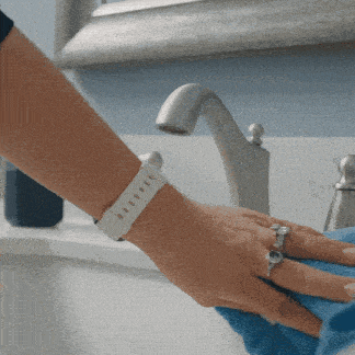 a woman wearing a white watch is cleaning a sink with a blue towel