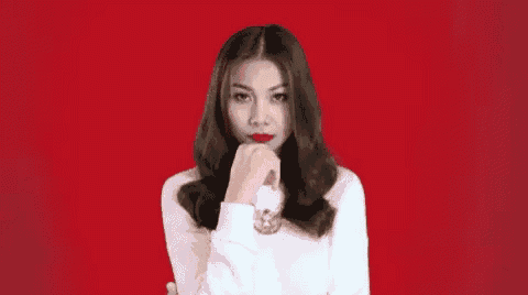 a woman in a white shirt is making a funny face with her hand on her chin .