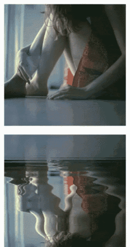 a woman in a red dress is sitting on the floor and her reflection is in the water