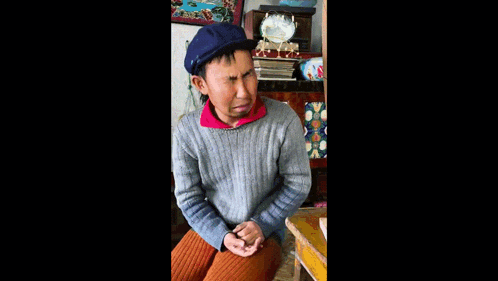 a man wearing a gray sweater and a blue hat is sitting in front of a clock