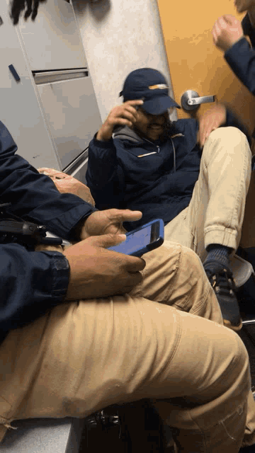 a man wearing a blue hat is sitting in a room with a phone in his hand