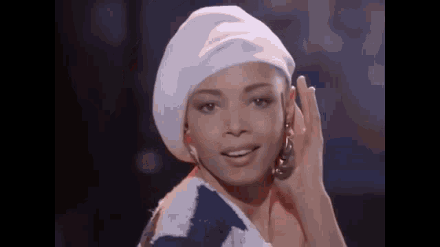 a woman wearing a white hat and a blue and white sweater is smiling and waving at the camera .