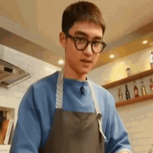 a young man wearing glasses and an apron is preparing food in a kitchen .