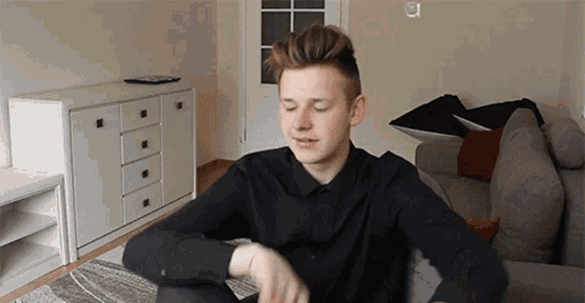a young man in a black shirt is sitting on a couch in a living room