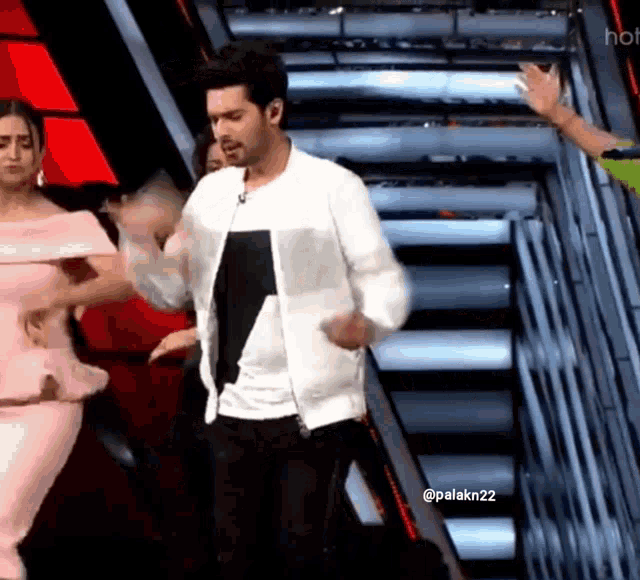 a man in a white jacket is dancing on a stage with two women behind him .
