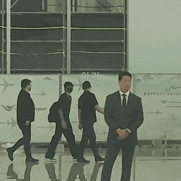 a man in a suit stands in front of a wall that says expect excelsior