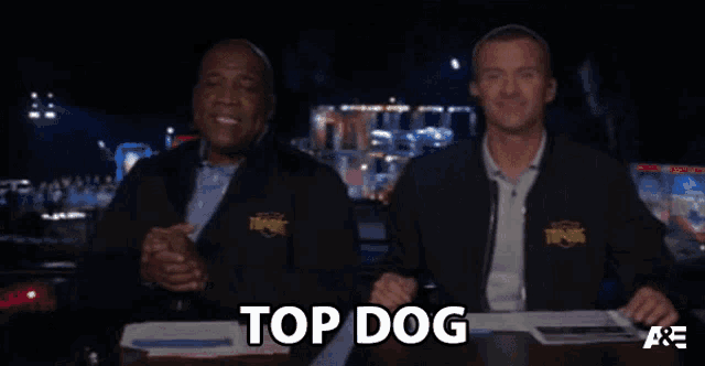 two men sitting at a table with the words top dog written on the screen