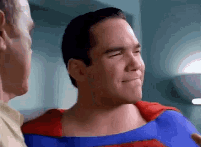 a man in a superman costume smiles while talking to another man