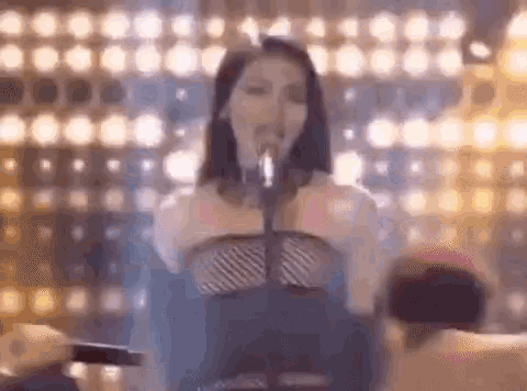 a woman is singing into a microphone on a stage in front of a crowd of people .