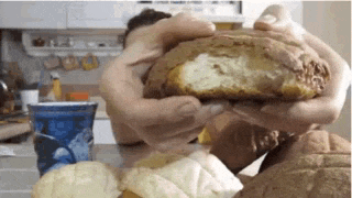 a person is holding a piece of bread in their hands while sitting at a table .