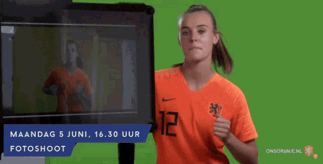 a woman wearing an orange shirt with the number 12 on it stands in front of a green screen