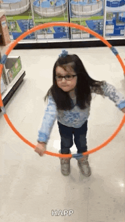a little girl wearing glasses is playing with an orange hula hoop in a store .