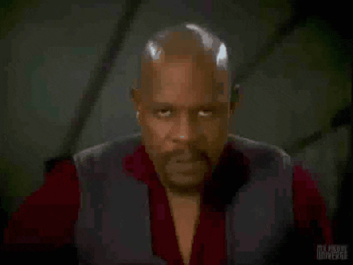 a man in a red shirt is holding a glass in front of his face and the word universe is on the bottom