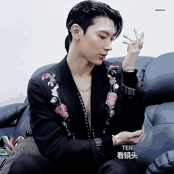 a man wearing a black jacket with pink flowers on the sleeves is sitting on a couch