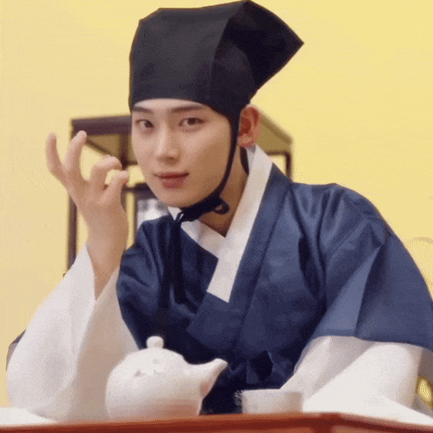 a man in a traditional costume is sitting at a table with a teapot and a cup .