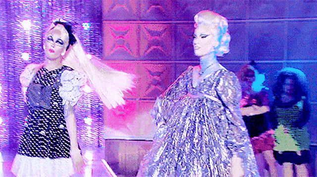 a couple of women are standing next to each other on a stage . one of the women is wearing a silver dress .