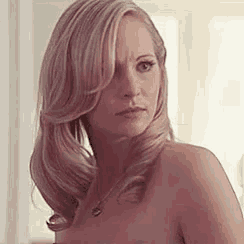 a naked woman with long blonde hair and a necklace on her neck is looking at the camera .