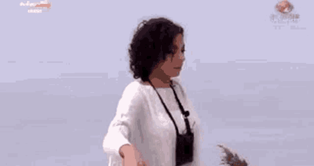 a woman is standing in front of a body of water wearing a white sweater .