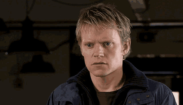 a man with blonde hair and blue eyes wears a blue jacket